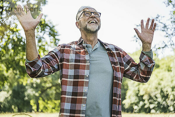 Fröhlicher älterer Mann mit erhobenen Armen steht im Park