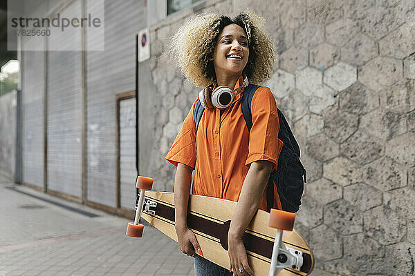 Junge Frau hält Skateboard in der Nähe der Wand