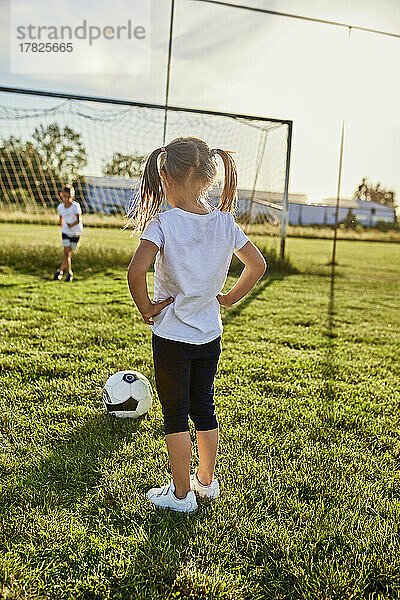 Girl standing with hand on hip in front of brother at sports field