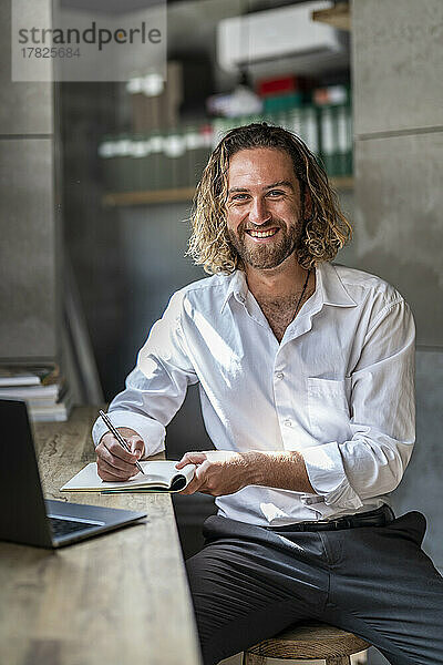 Lächelnder Geschäftsmann mit Stift und Tagebuch im Büro