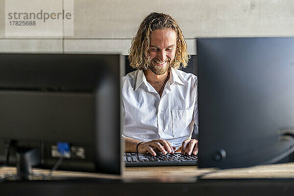 Lächelnde Führungskraft nutzt Desktop-PC am Schreibtisch im Büro