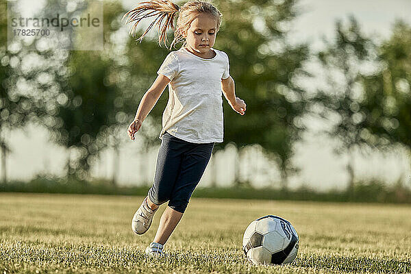Blond girl playing soccer at sports field on sunny day