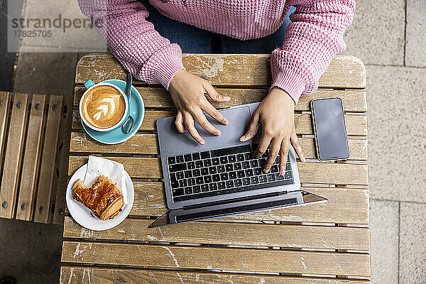 Young woman using laptop sitting at sidewalk cafe