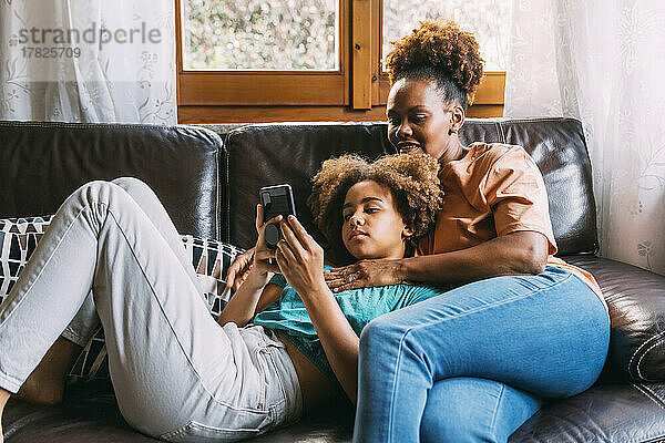 Mädchen teilt Smartphone mit Mutter auf Sofa zu Hause