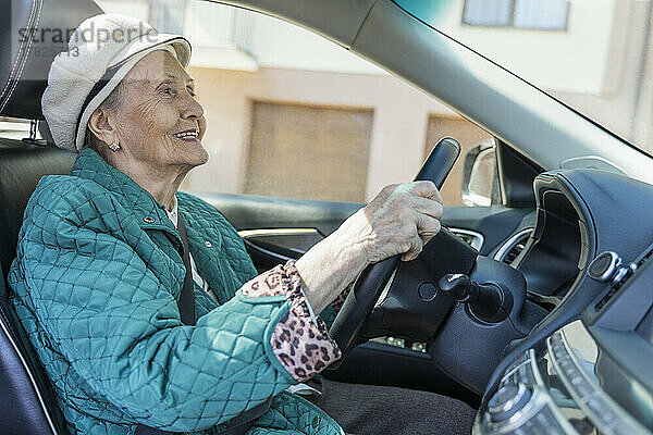 Lächelnde ältere Frau mit Baskenmütze  die Auto fährt