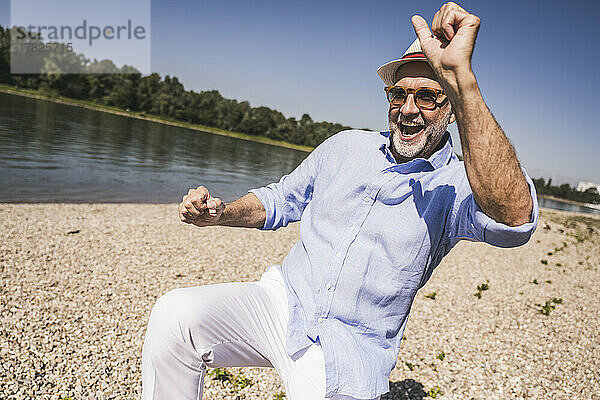 Glücklicher älterer Mann  der an einem sonnigen Tag am Flussufer tanzt