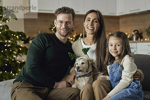 Lächelnde Familie mit Hund sitzt auf dem Sofa im Wohnzimmer