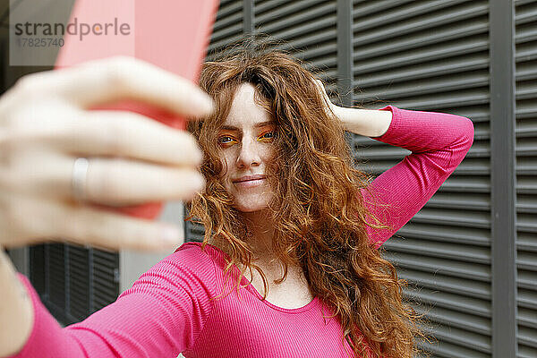 Lächelnde Frau mit der Hand im Haar macht ein Selfie per Smartphone
