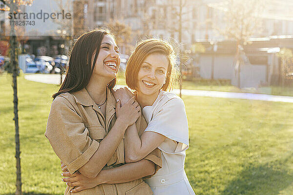 Glückliche Frau umarmt fröhliche Freundin im Park an einem sonnigen Tag