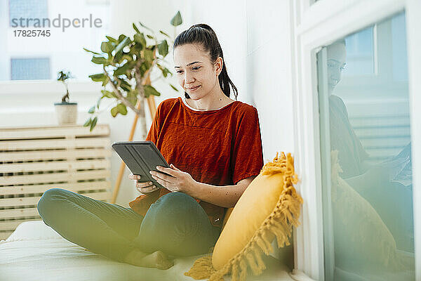 Lächelnde Frau mit Tablet-PC  die zu Hause auf dem Sofa sitzt