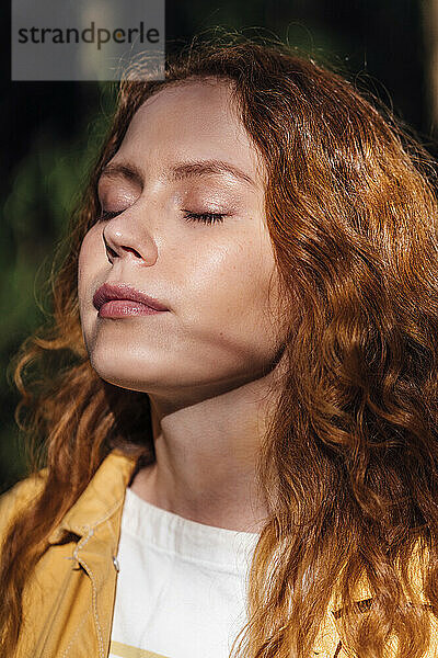 Redhead woman with eyes closed enjoying sunlight