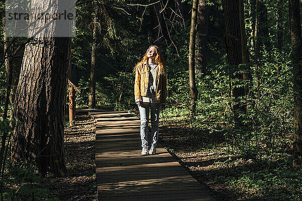 Junge Frau mit geschlossenen Augen geht auf Fußweg im Wald