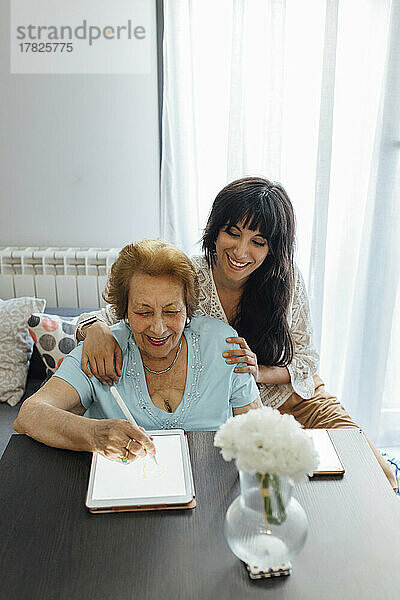 Glückliche Frau mit Großmutter  die zu Hause einen Tablet-PC nutzt