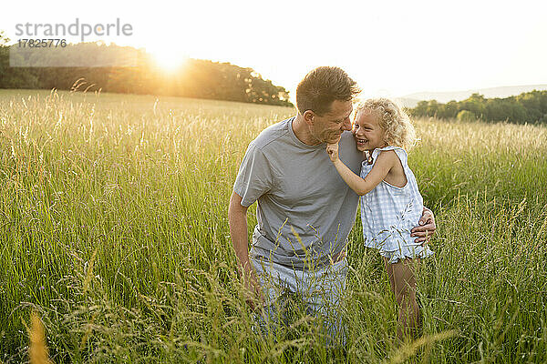 Happy girl standing by father kneeling on grass at field