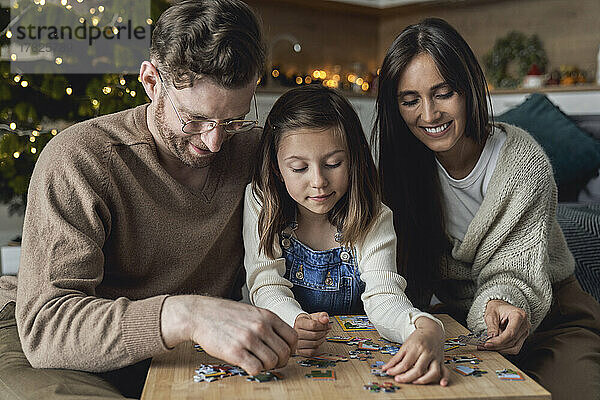 Smiling parents with daughter joining puzzle at home