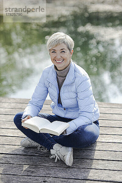 Glückliche Frau mit Buch sitzt am Pier