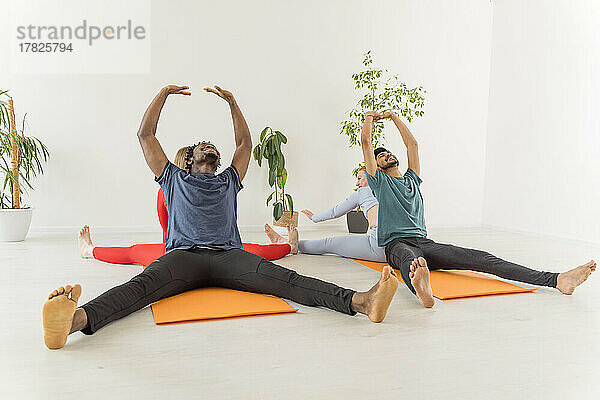 Gemischtrassige Paare üben gemeinsam Dehnübungen im Yoga-Studio