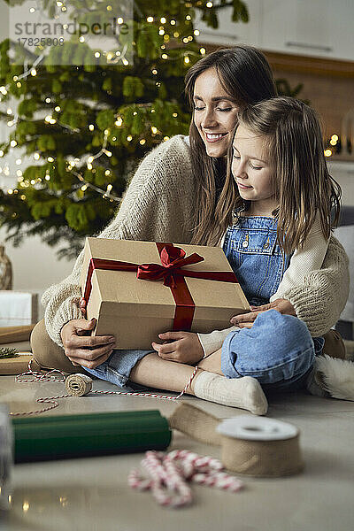 Lächelnde Mutter umarmt Tochter mit Weihnachtsgeschenk zu Hause