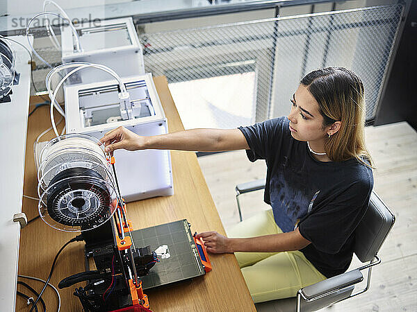 Junger Techniker justiert Filamentrolle auf 3D-Drucker in der Werkstatt