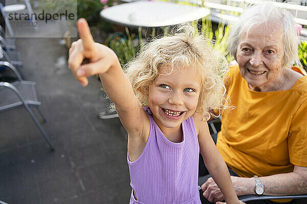 Glückliche Seniorin blickt auf ihre Enkelin und zeigt auf den Balkon