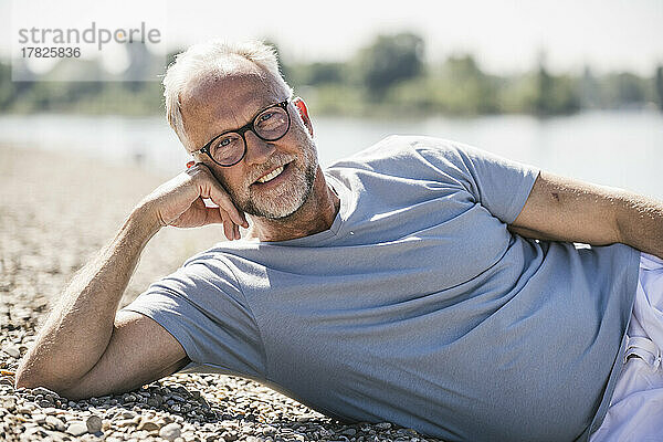 Lächelnder Mann  der an einem sonnigen Tag am Flussufer liegt