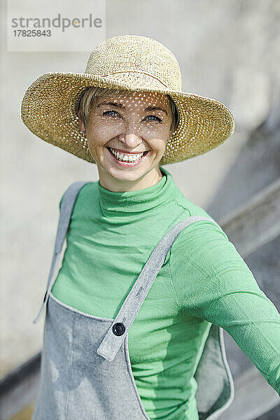 Glückliche Frau mit Hut steht an einem sonnigen Tag