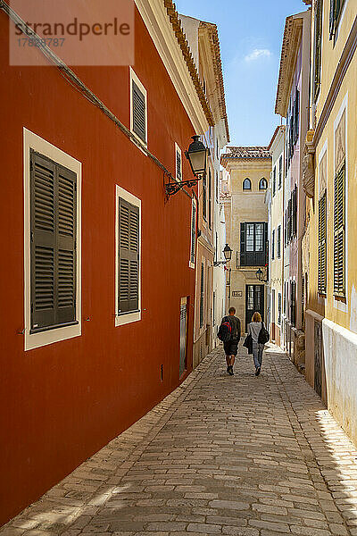 Blick auf ein Paar  das eine pastellfarbene Straße im historischen Zentrum entlanggeht  Ciutadella  Menorca  Balearen  Spanien  Mittelmeer  Europa