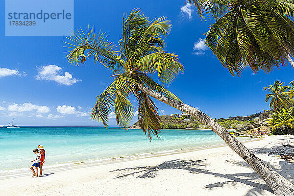 Fröhlicher kleiner Junge mit Mutter beim Spaziergang am idyllischen Palmenstrand  Antigua  Leeward Islands  Westindien  Karibik  Mittelamerika