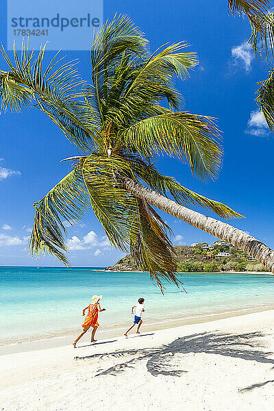 Frau und kleiner Junge haben Spaß beim Laufen an einem palmengesäumten Strand  Antigua  Westindien  Karibik  Mittelamerika