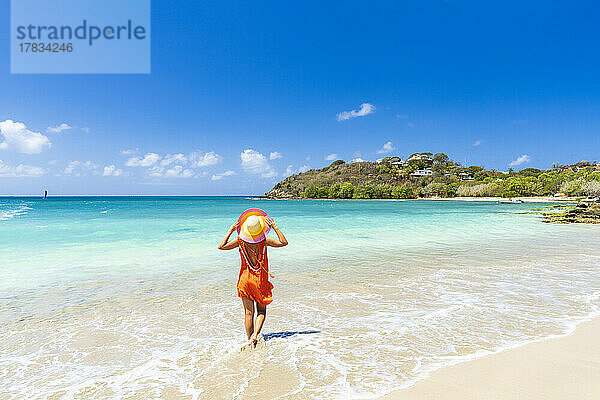 Schöne Frau mit orangefarbenem Kleid und Strohhut an einem tropischen Strand  Antigua  Westindien  Karibik  Mittelamerika