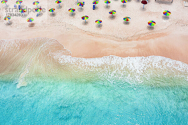 Mehrfarbige Sonnenschirme am tropischen Strand  umspült von den Wellen des Karibischen Meeres  Luftaufnahme  Antigua  Westindien  Karibik  Mittelamerika