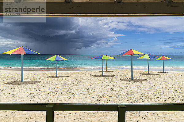 Mehrfarbig gestreifte Sonnenschirme am weißen Sandstrand unter Gewitterwolken  Antigua  Westindien  Karibik  Mittelamerika