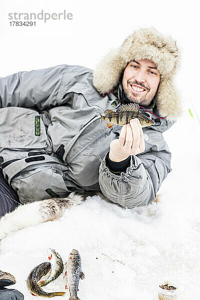 Porträt eines lächelnden Mannes  der einen nach dem Eisfischen gefangenen Fisch hält  Lappland  Schweden  Skandinavien  Europa