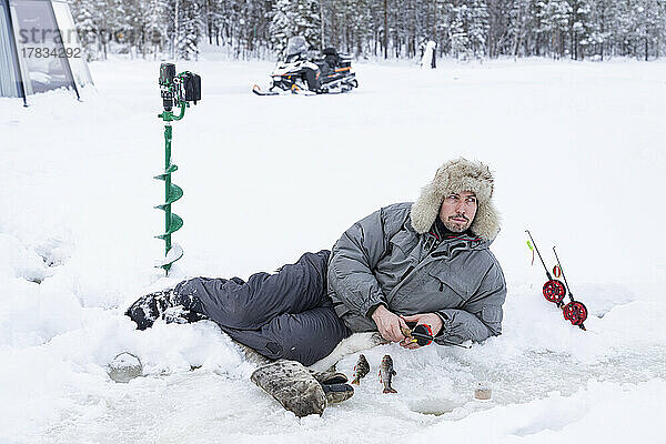 Mann liegt auf dem Eis und angelt aus einem Loch  Lappland  Schweden  Skandinavien  Europa