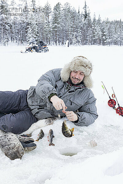 Fröhlicher Mann  der den Fischfang aus dem Eisloch aufnimmt  Lappland  Schweden  Skandinavien  Europa