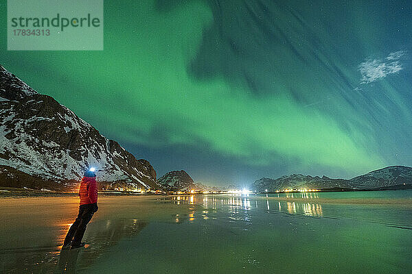 Wanderer mit Stirnlampe bei der Beobachtung der Aurora Borealis (Nordlichter) am Strand von Ramberg  Provinz Nordland  Lofoten  Norwegen  Skandinavien  Europa