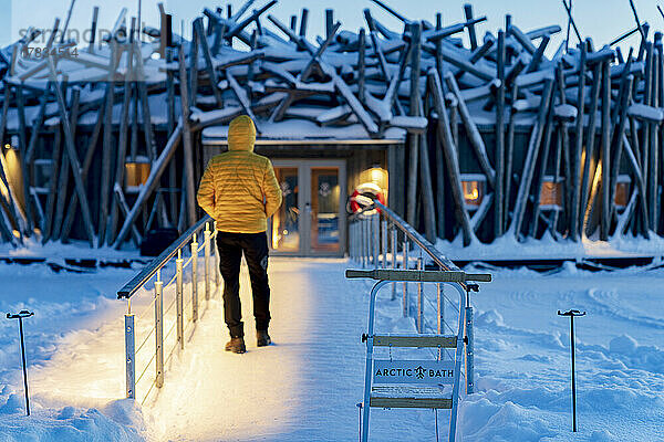 Person  die in der Abenddämmerung auf dem gefrorenen Steg steht  der das schwimmende Arctic Bath Hotel mit dem Ufer verbindet  Harads  Lappland  Schweden  Skandinavien  Europa