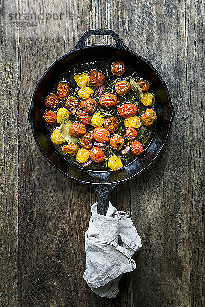 Bunte  geröstete Tomaten in einer Pfanne mit Kräutern und Knoblauchzehen