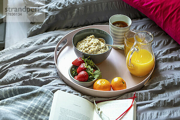 Frühstückstablett mit Porridge  Tee  Orangensaft und Obst auf Bett
