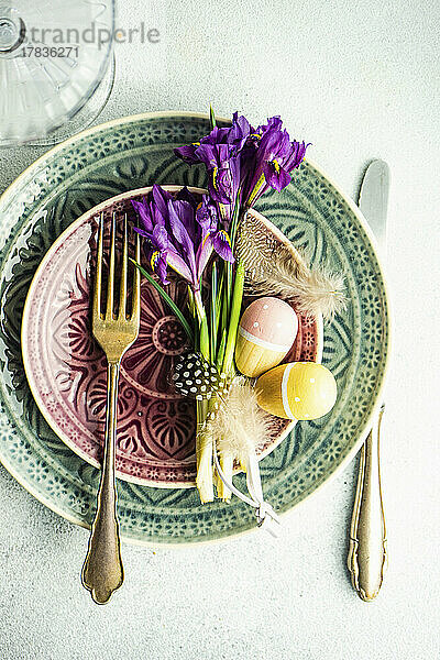 Ostergedeck mit Keramiktellern  Iris  Eiern und Federn auf Betontisch