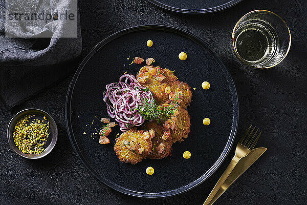 Mini-Lachspuffer mit Zwiebelsalat auf schwarzen Teller  mit goldenem Besteck