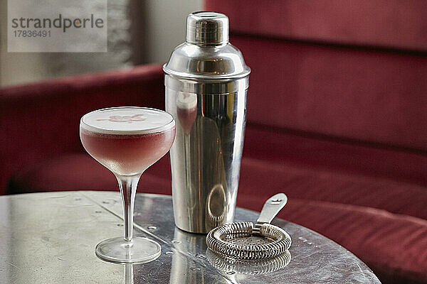 Rosa Cocktail in einem Martini-Glas dahinter Cocktailshaker