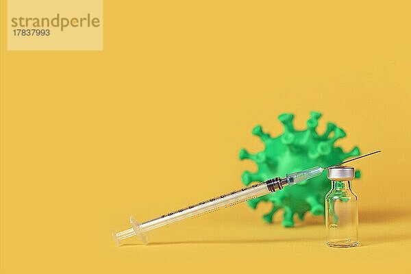 Corona-Impfstoff Ampulle mit Spritze und Virus-Modell im Hintergrund auf gelbem Hintergrund mit Kopie Raum