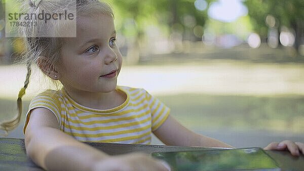 Niedliches kleines Mädchen hört Musik auf einem Mobiltelefon und singt mit. Nahaufnahme eines kleinen Mädchens  das im Stadtpark sitzt und mit dem Handy Musik hört. Odessa  Ukraine  Europa