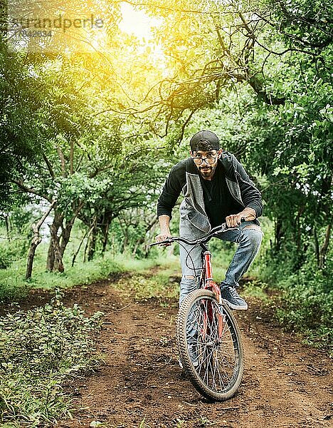 Ein Mann  der auf dem Land Fahrrad fährt  Person  die auf dem Land Fahrrad fährt  Porträt eines Mannes mit Mütze  der auf einer Landstraße Fahrrad fährt  Fahrradfahrer auf seinem Fahrrad auf einer Landstraße Wald