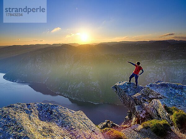 Frau steht auf einer Felsnase am Kjerag über dem Lysefjord und zeigt mit dem Finger in die Ferne  Sonnenuntergang  Lyseboten  Rogaland  Norwegen  Europa