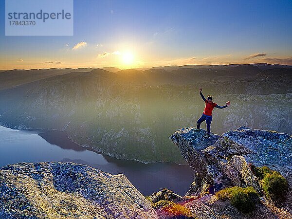 Frau steht mit gespreitzten Armen auf einer Felsnase am Kjerag über dem Lysefjord  Sonnenuntergang  Lyseboten  Rogaland  Norwegen  Europa