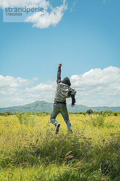 Konzept einer freien Person  die springt und den Arm hebt  Freie Person  die mit Freude auf dem Feld springt  Mann von hinten  der auf einem schönen Feld springt  Rückansicht eines Mannes  der im Gras springt und die Faust hebt