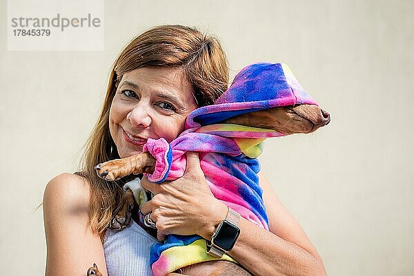 Lateinamerikanische Frau hält ihren Hund  beide gleich gekleidet. Sie schaut in die Kamera