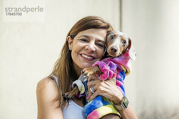 Lateinamerikanische Frau hält ihren Hund. Beide sind gleich gekleidet und schauen in die Kamera